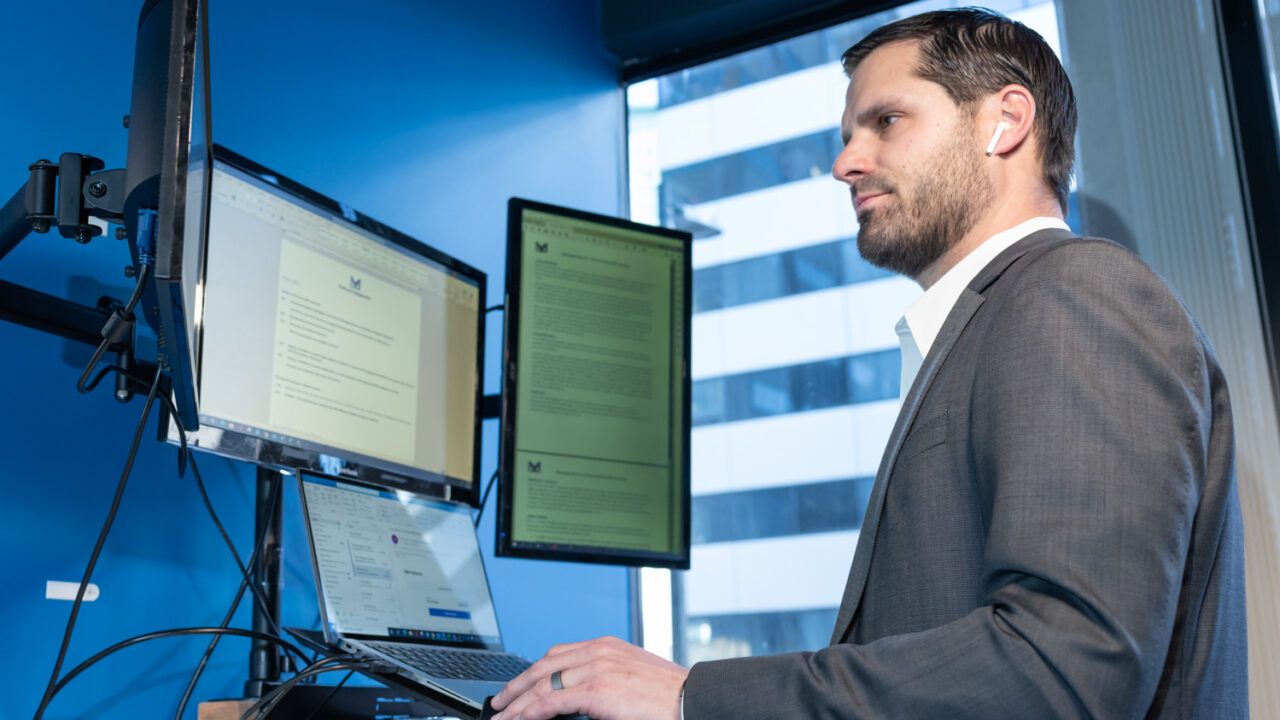 Man at standing desk with three monitors, working intently