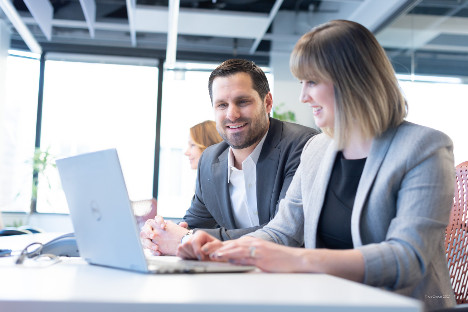 Two colleagues in suits smiling at a laptop screen