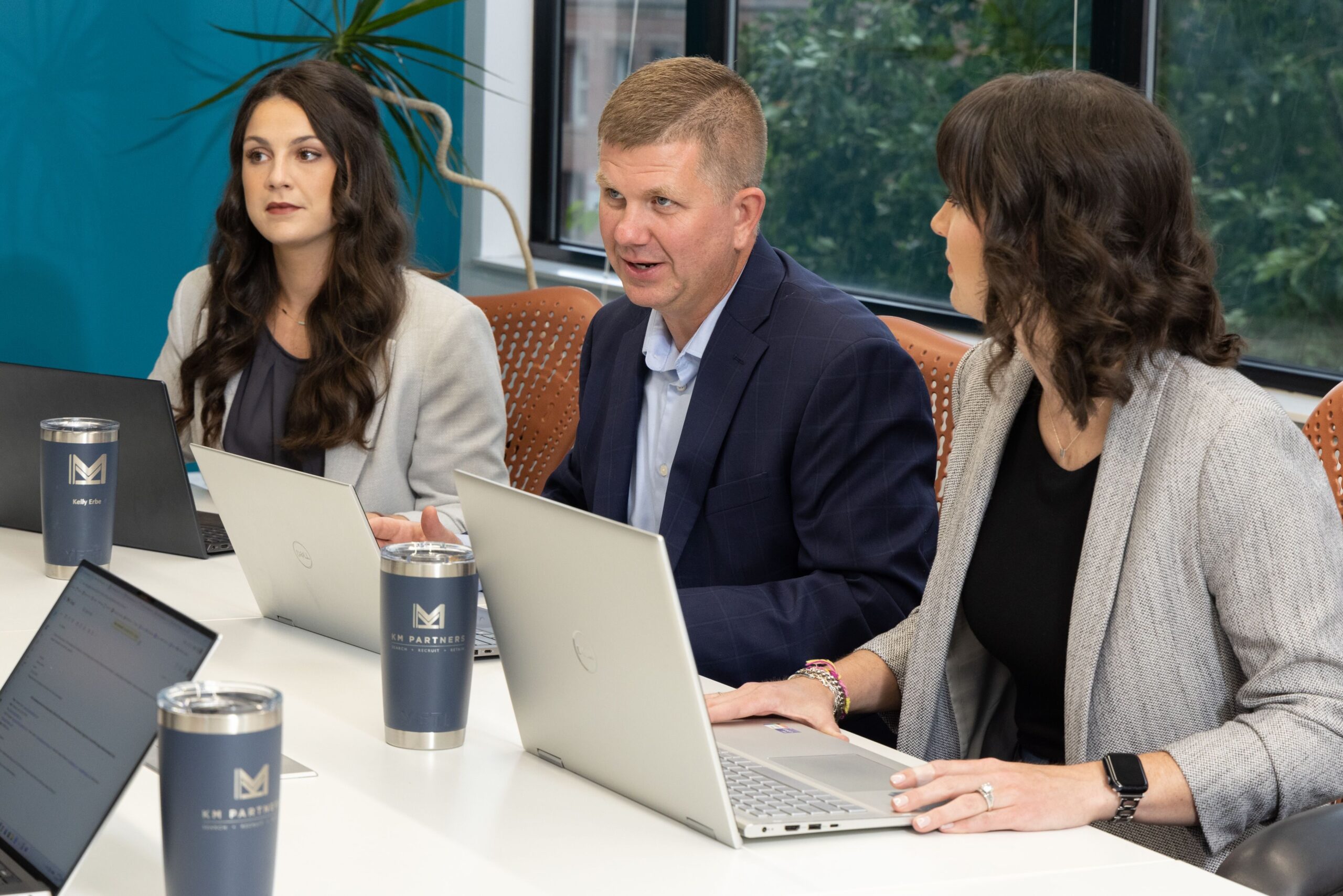 Three people in a meeting with laptops, engaged in discussion