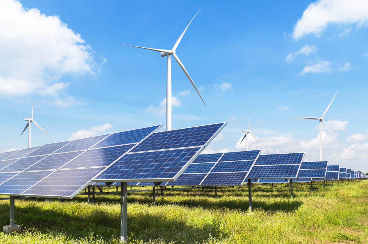 Solar panels and wind turbines in a green field under a clear blue sky